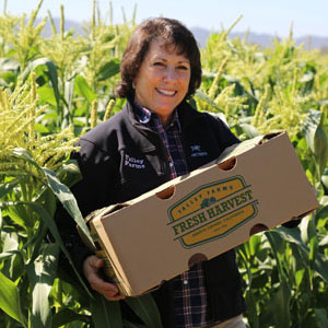 Andrea Chavez poses with boxed produce in a corn field