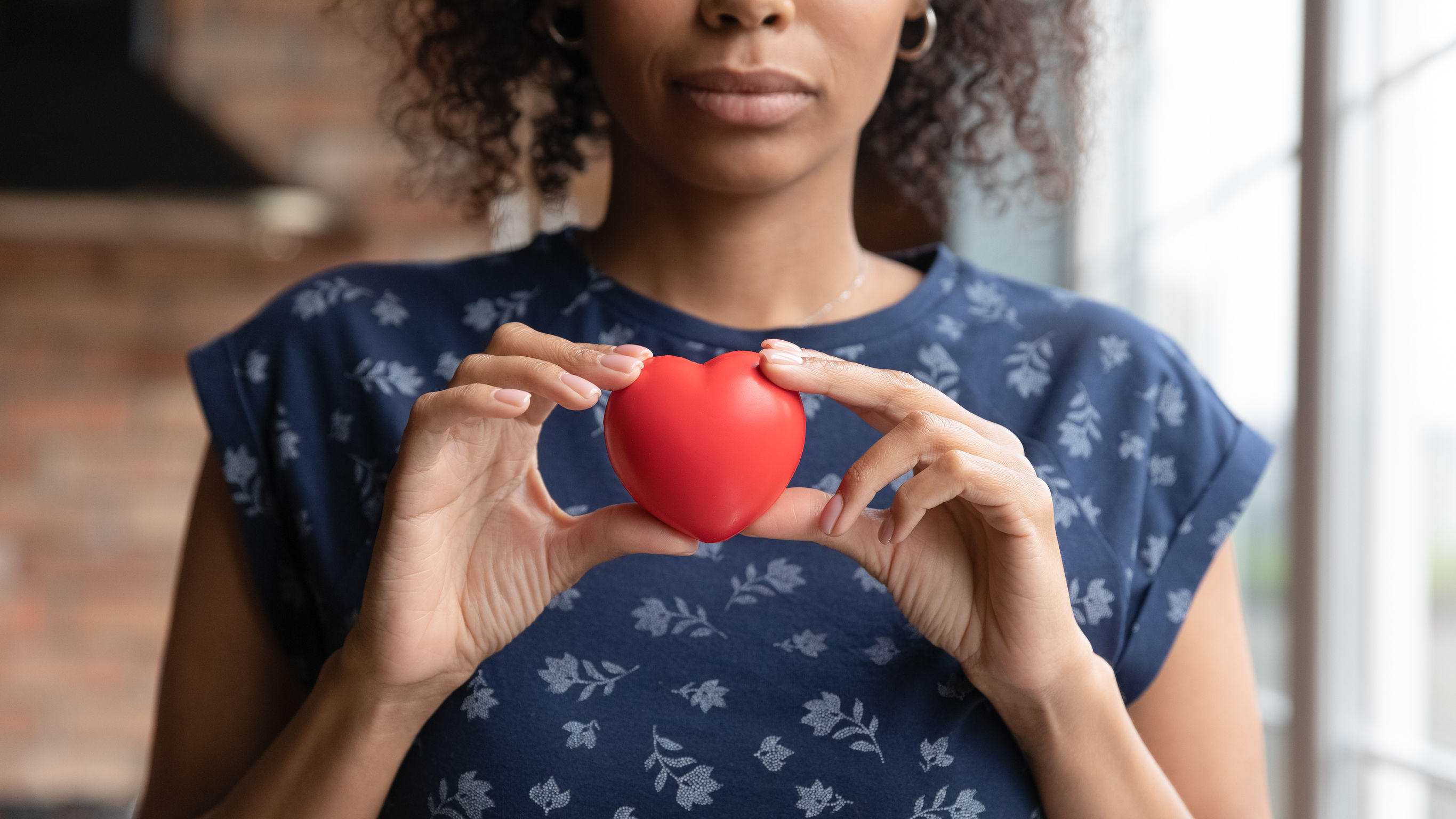 A close cropped image of a woman holding a small red toy heart