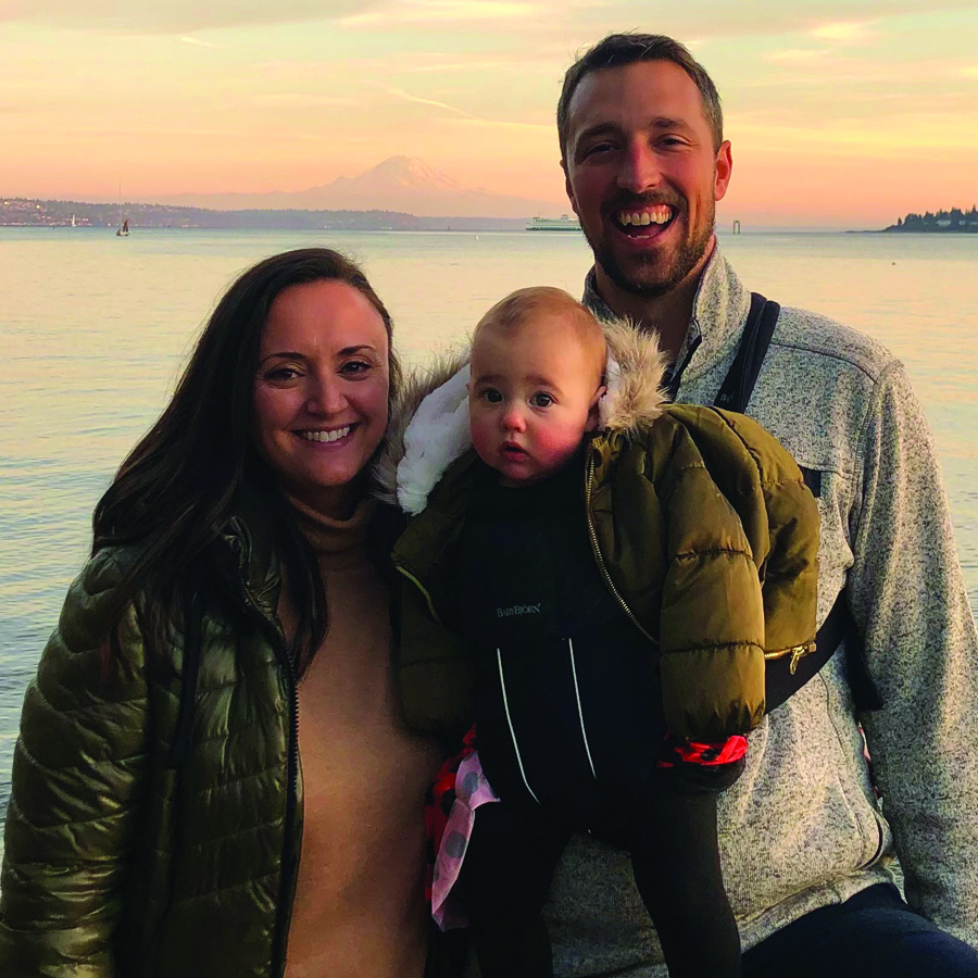 A couple and their young baby by the shoreline at sunset.